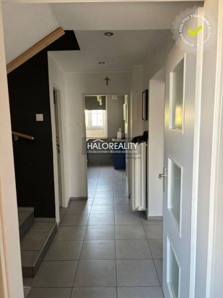 A hallway of a family house with white walls, tiles, and a view of the kitchen.