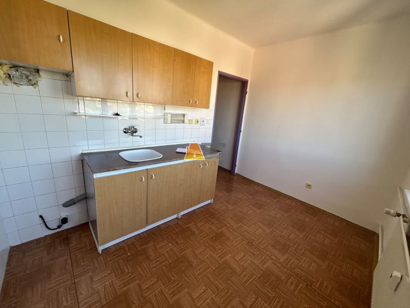 A kitchen in a 2-room apartment with a wooden decor floor and a kitchen unit.