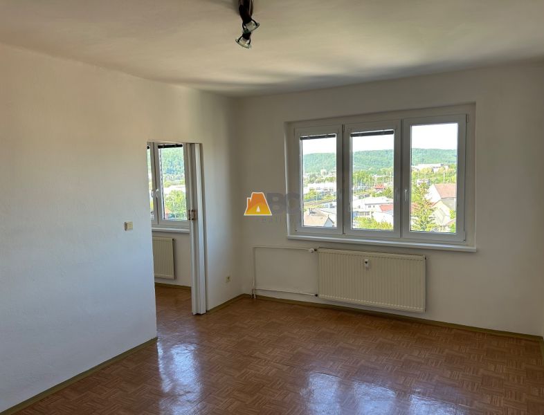 A bright room with three windows and a wooden decor floor in a two-room apartment.