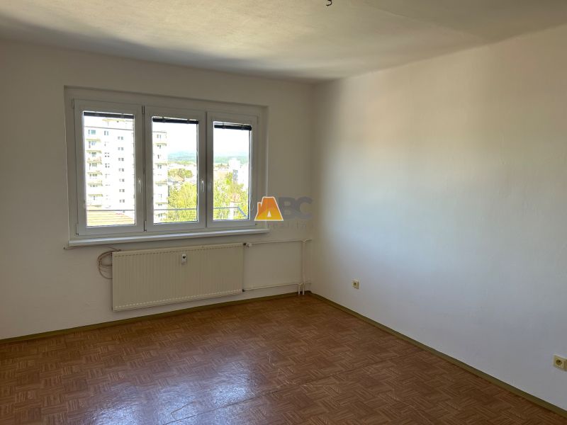 A room in a 2-room apartment with a wooden decor floor and a large window.
