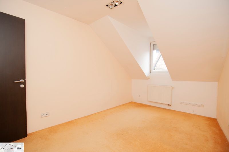 An empty room with a colorful carpet, a radiator, and a bright window in a 3-room apartment.