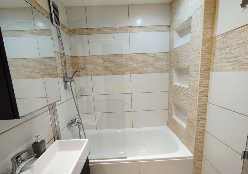 A bathroom in a one-room apartment with a bathtub, shower, and ceramic tiles on the walls.