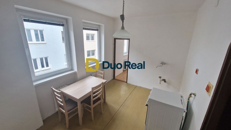 A dining room with a wooden table and chairs in a 3-room apartment, with two windows and light.