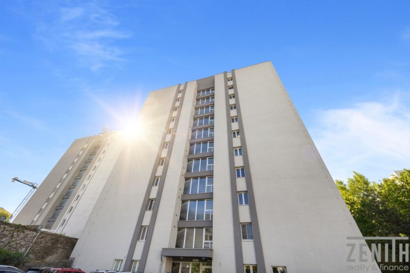 A high-rise apartment building in Bratislava - Old Town with a blue sky and a parking lot.