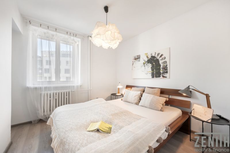 A bright bedroom with a wooden bed, a painting on the wall, and a floor with a wooden decor.