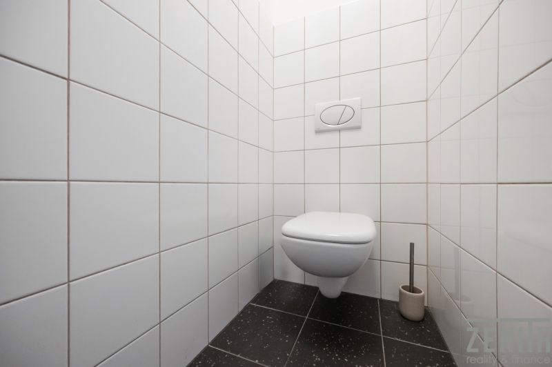 A toilet with white tiles and a black floor in a two-room apartment.