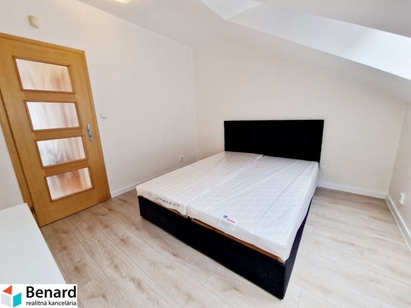A bedroom in a three-room apartment with a wood-patterned floor and a simple bed.