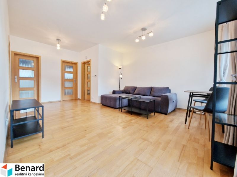 A room of a three-room apartment with a wooden decor floor, a gray sofa, and a table.