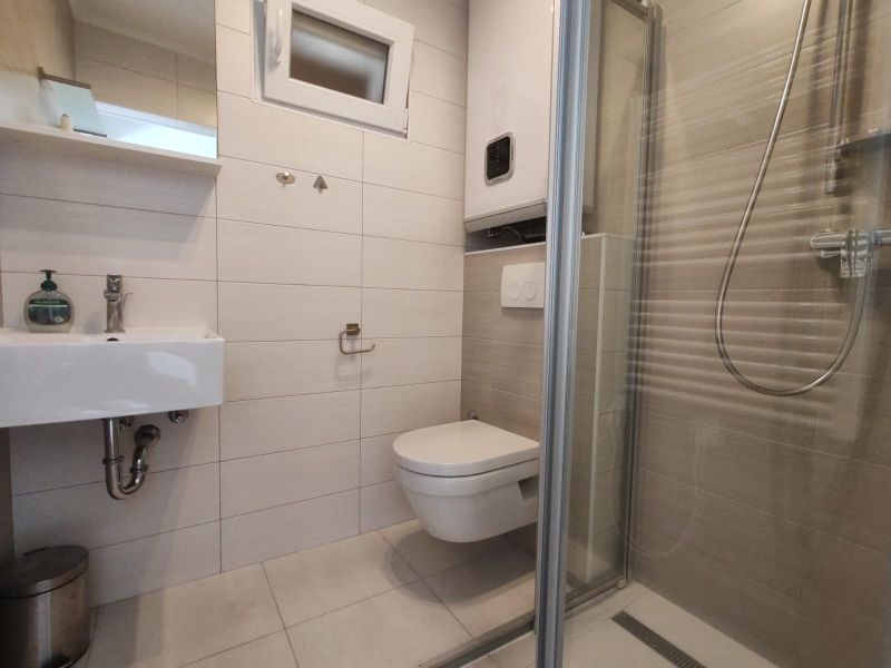 A bathroom in a family house with a sink, shower corner, and wall-mounted toilet.