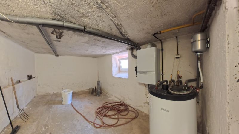 A technical room with a boiler in a family house, simple equipment, pipes, window, tools.