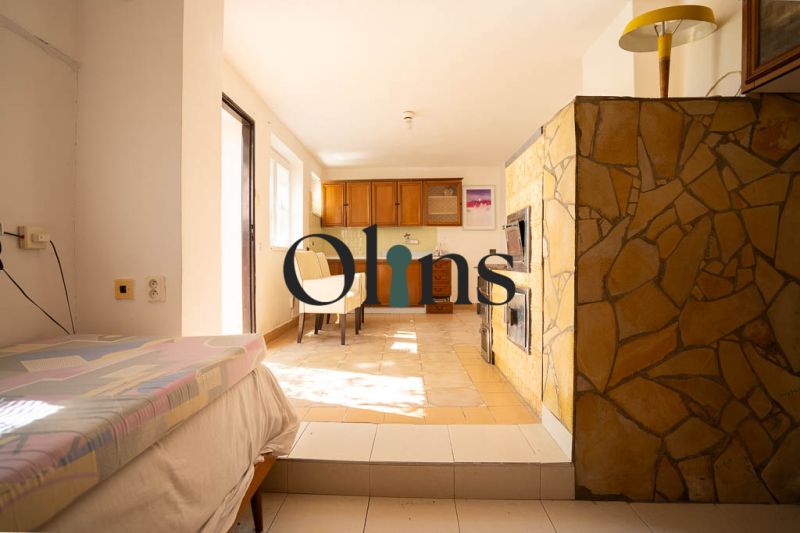 Interior in a family house with a fireplace, bed, kitchen cabinets, and table.