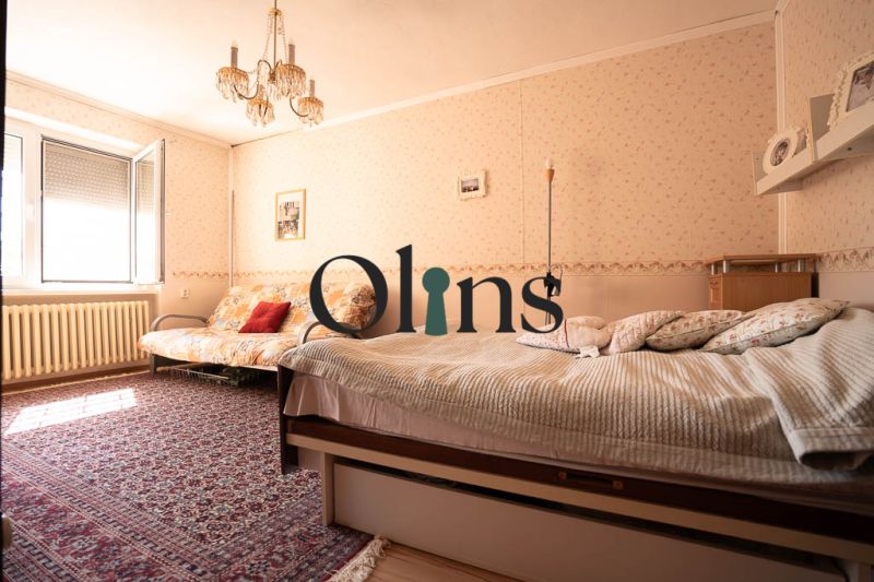 A bedroom in a family house with a carpet, bed, sofa, and chandelier.