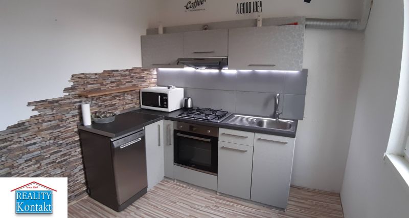 A kitchen in a 2-room apartment with a wooden decor floor and a stone wall.