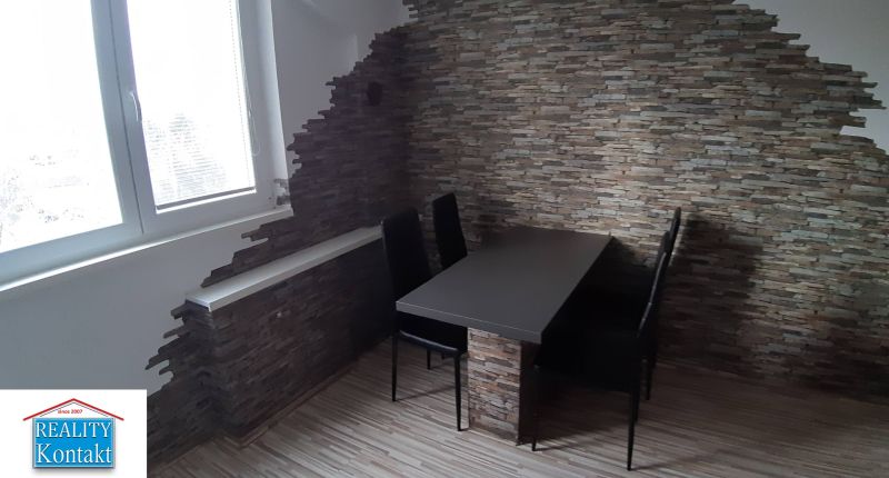Dining area with a table and chairs in a 2-room apartment, stone wall.