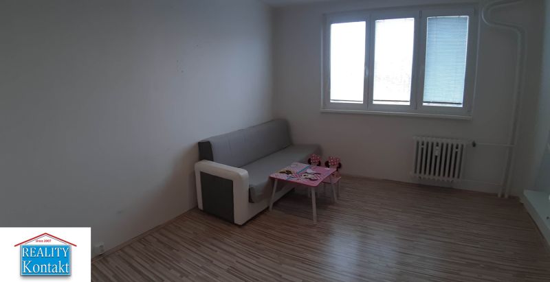 Living room in a two-room apartment with a couch and a table, wooden decor flooring.