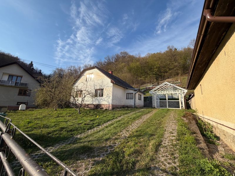 A family house in Štós surrounded by greenery and a wooden structure of a shelter.