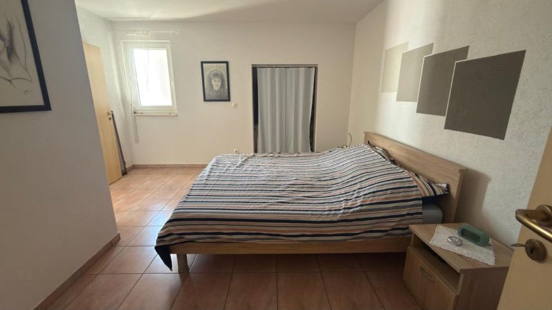 A bedroom in a family house with a bed, ceramic flooring, and minimalist decor.