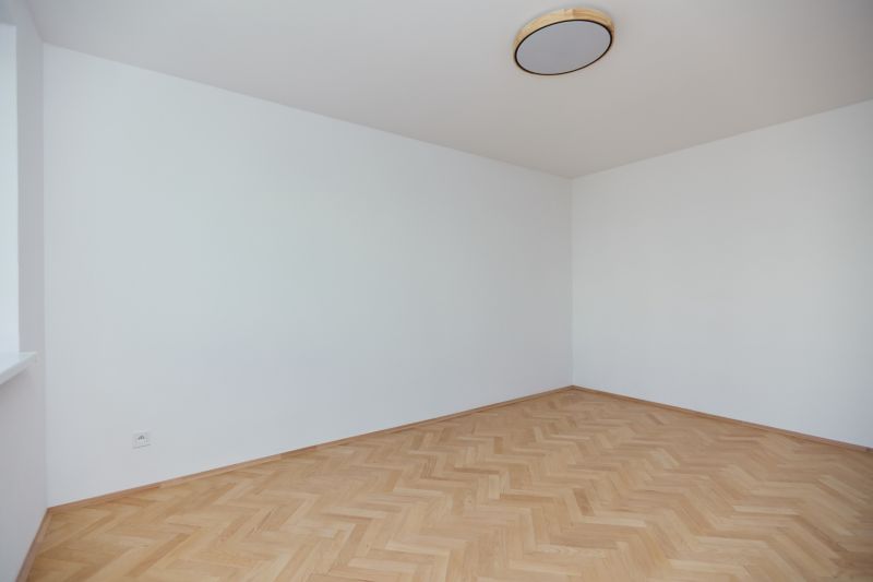 An empty room with white walls and a wooden decor floor in a 3-room apartment.