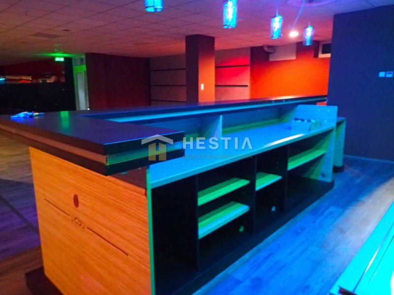 A bar counter in commercial premises with ceiling lighting, wooden and colorful flooring.