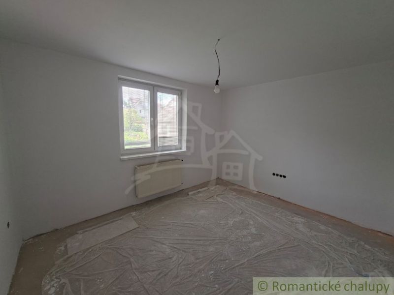 An empty room with a plastic window, a radiator, and an exposed ceiling light in a family house.