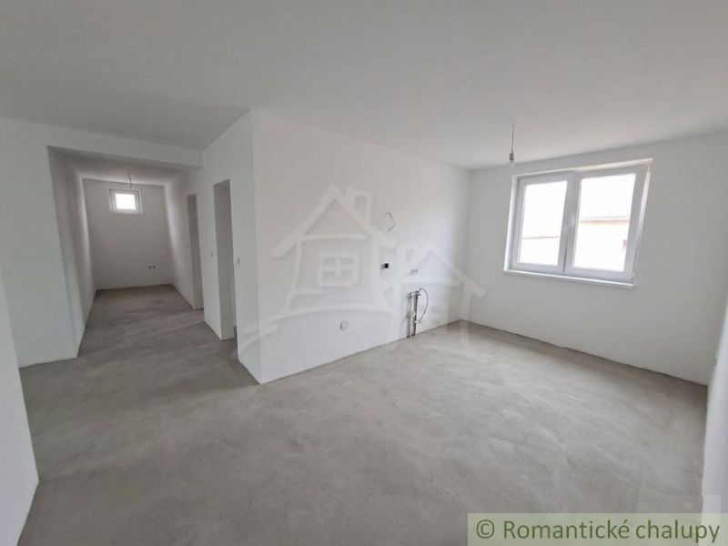White room with a window, concrete floor, outlets for a kitchen unit in a family house.