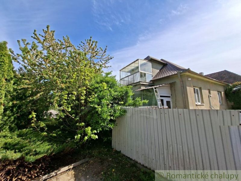 A family house in Orešany surrounded by greenery with a metal fence in the foreground.