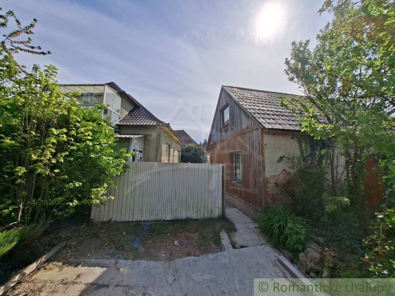A family house in Orešany with two buildings, surrounded by lush greenery and a wooden fence.