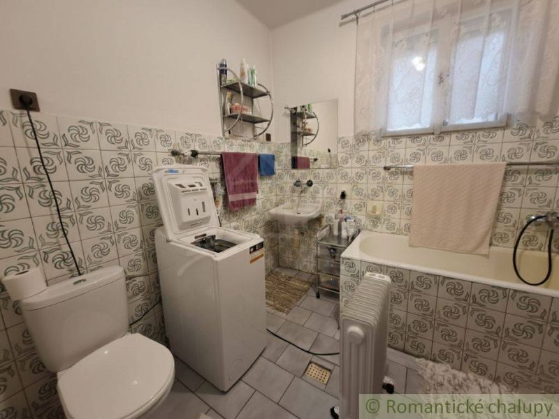 A bathroom in a family house with a washing machine, a bathtub, and tiles with a floral pattern.