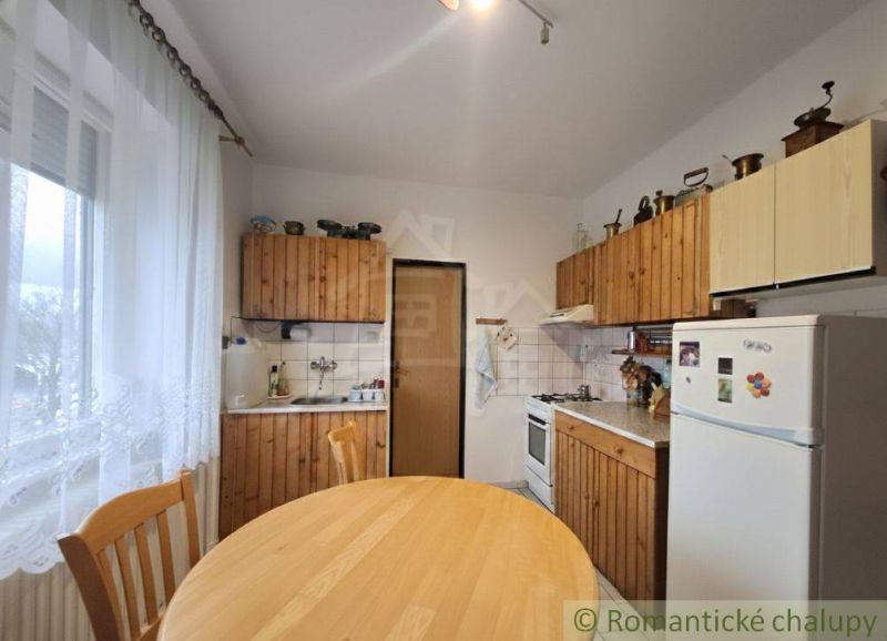 A kitchen in a family house with wooden cabinets, a dining table, a refrigerator, chairs.