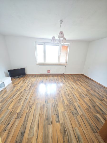 A spacious living room with a wooden decor floor and a large window in a 3-room apartment.