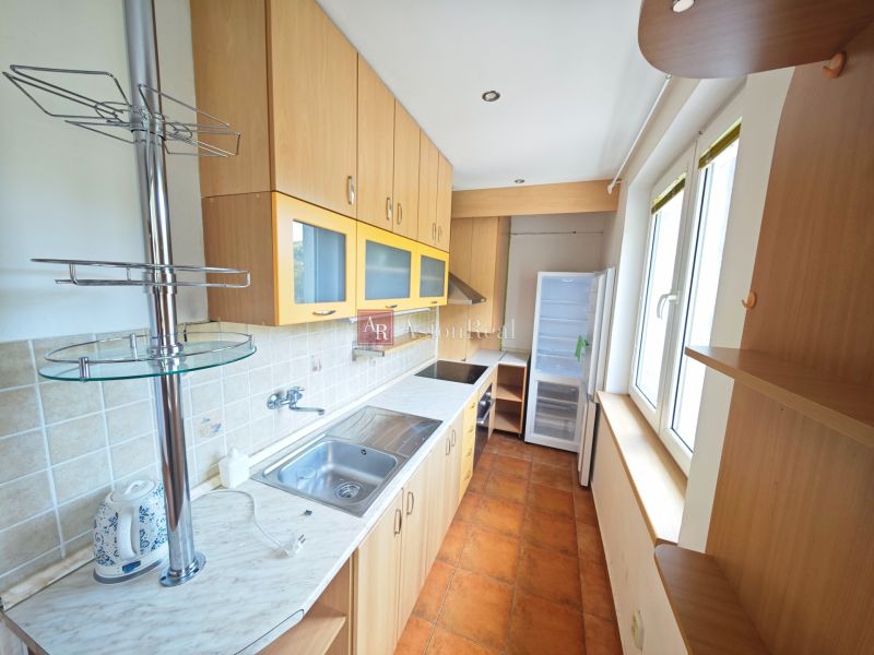 A kitchen in a 3-room apartment with a cooktop, cabinets, and windows, and a floor with a wooden decor.