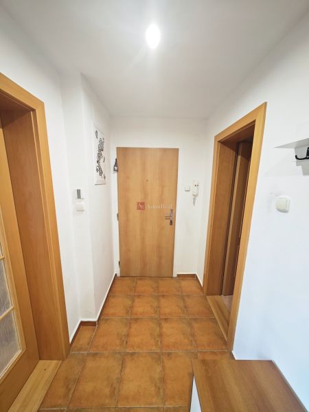 A hallway in a 3-room apartment with ceramic tiles, white walls, and wooden doors.