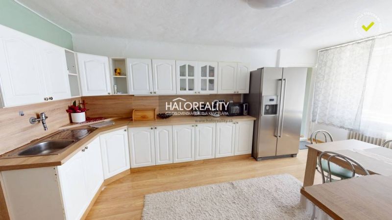 A kitchen in a family house with white cabinets, a refrigerator, and a wooden-patterned floor.