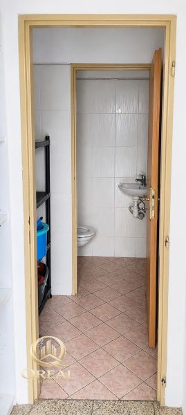 A bathroom in commercial premises with a toilet and a sink, simple tile design.