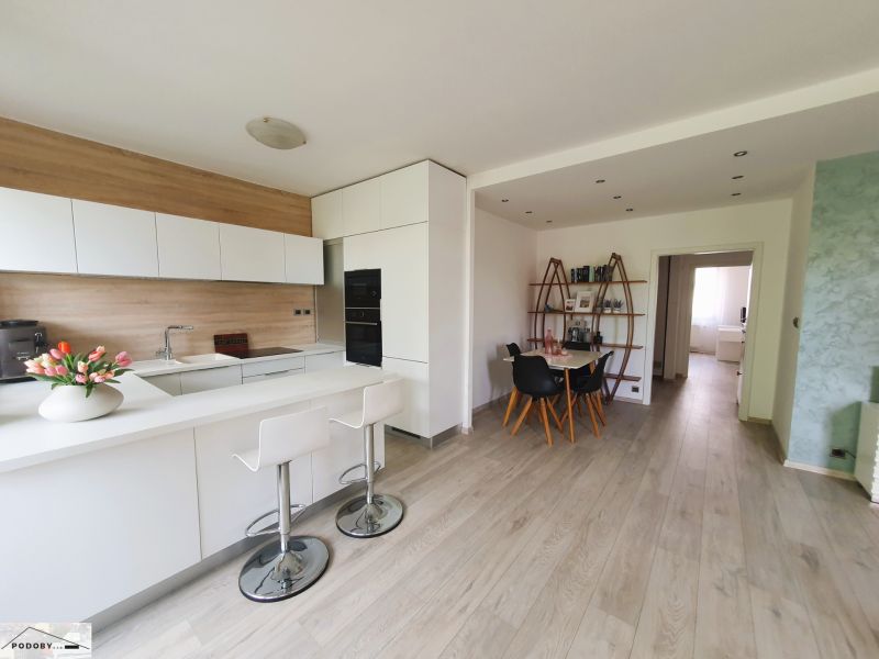 A kitchen with a dining area, white cabinets, and a wood-patterned floor in a three-room apartment.