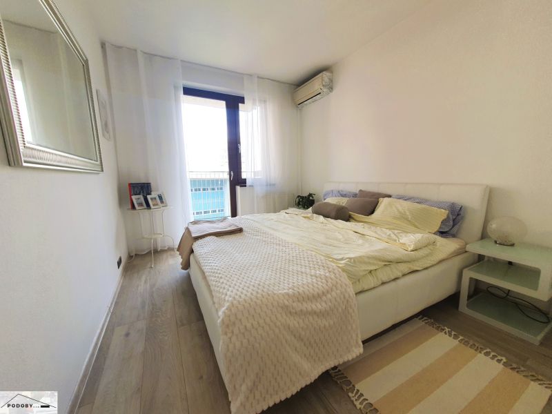 A bright bedroom with wood-patterned flooring in a three-room apartment.