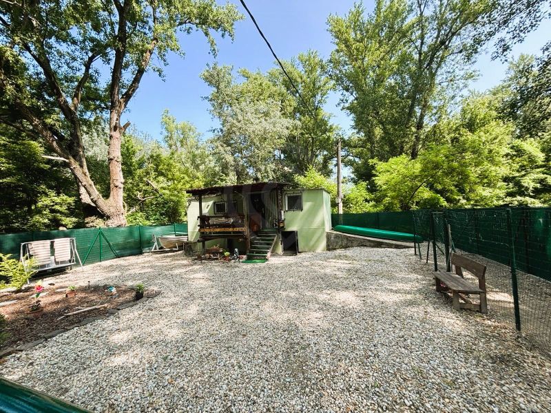 A cottage in Gabčíkovo with two benches in a yard surrounded by trees.