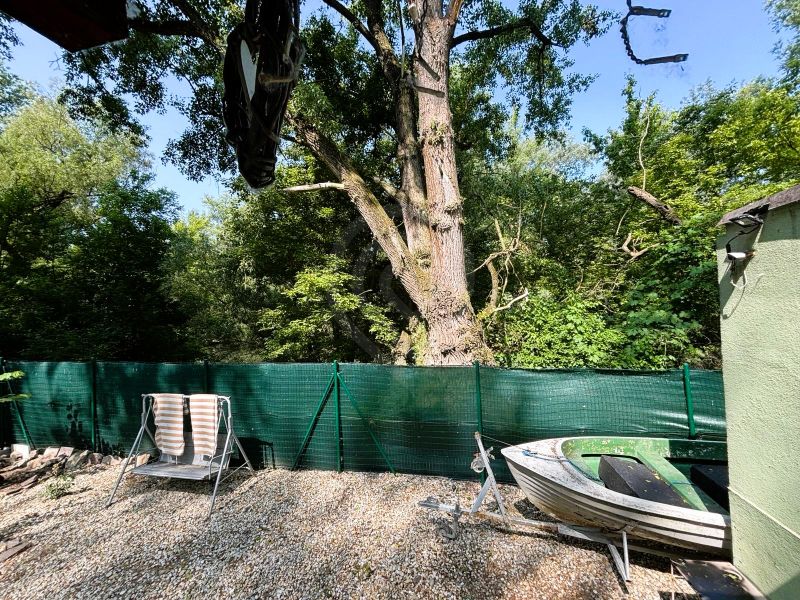 The yard of the cottage in Gabčíkovo with a deck chair, a boat, and a forest scene.