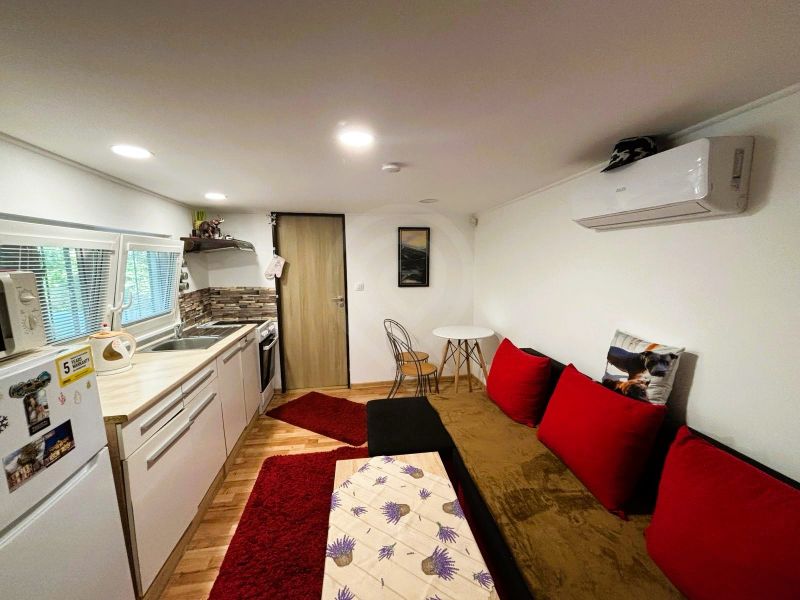 Interior of a cottage with a kitchen, red cushions, and a wooden decor floor.