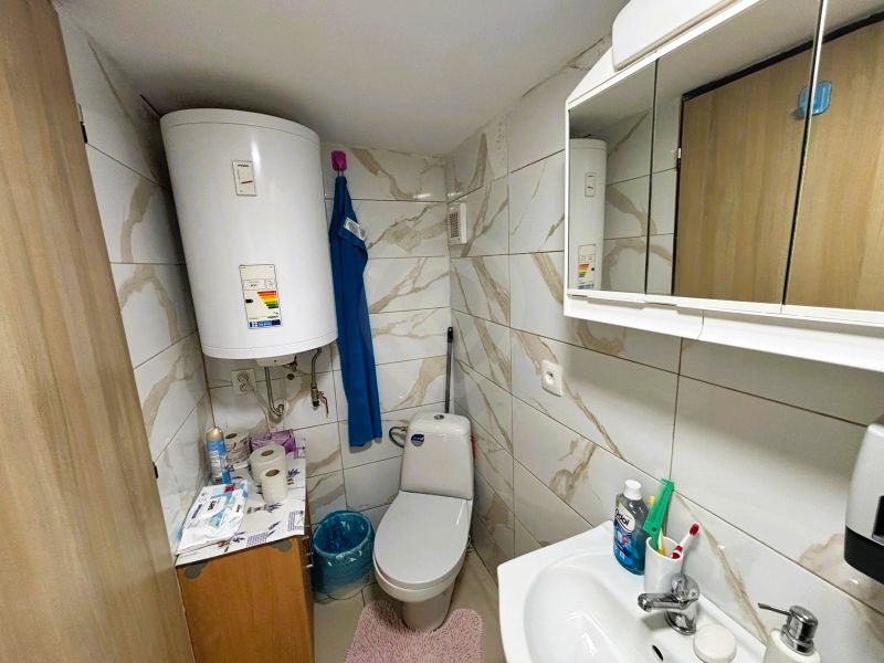 A bathroom with tiles and a boiler offers basic hygiene supplies and storage space.