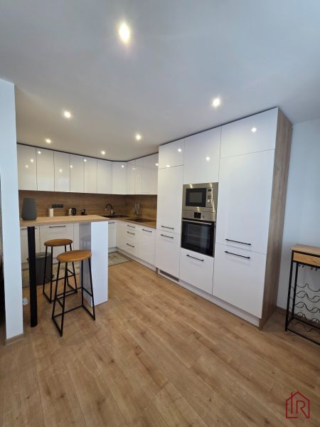 A kitchen in a 3-room apartment with bar seating and a floor with a wooden decor.