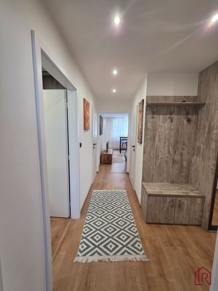 A hallway in a 3-room apartment with a wooden decor floor and a carpet with a geometric pattern.