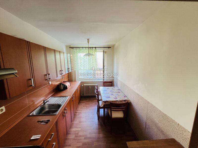 A kitchen in a 3-room apartment with a wooden decor floor, light furniture, and a dining table.