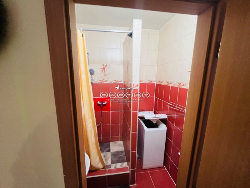 A bathroom in a 3-room apartment with a washing machine, shower, and red tiles.