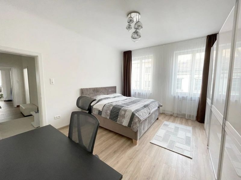 A bright bedroom with wood-patterned flooring and a desk in a three-room apartment.