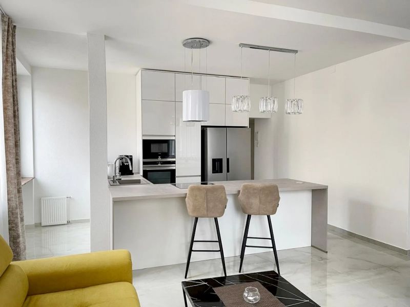 A kitchen in a 3-room apartment with an island, bar stools, and light cabinets.