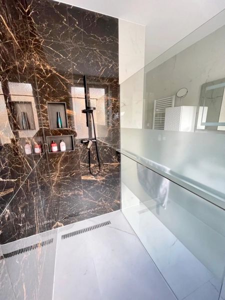 A shower corner in a 3-room apartment with black marble tiles and a glass partition.