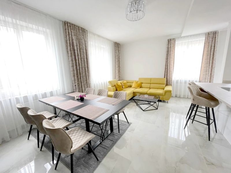 A bright living room with a dining table, a yellow sofa, and bar stools in a three-room apartment.
