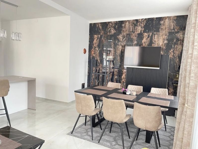 Dining room with a table and six chairs, wooden decor flooring, TV on the wall.