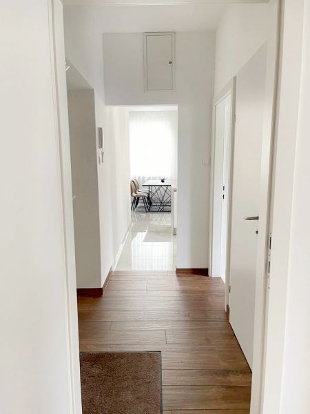 The hallway of the 3-room apartment with a wooden decor floor leads to the dining room.